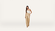 Woman in a white tank top and gold sequin wide-leg pants poses confidently against a plain white background.