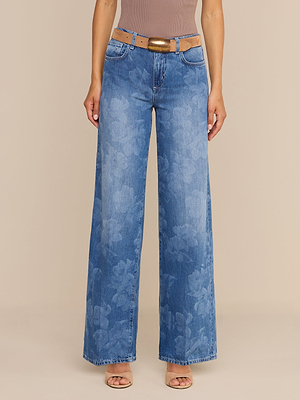 A person wears the Alicent Wide-Leg Jean in a sneaker length with a floral print, styled with a tan belt and open-toed beige heels. The upper body is partially visible against a plain beige background.