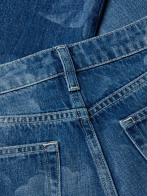 Close-up of the Alicent Wide-Leg Jean in blue denim, highlighting the waistband, belt loop, stitching details, and back pockets with another denim fabric partially visible in the background.