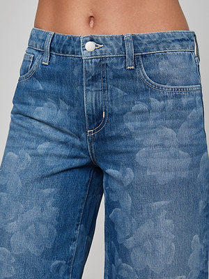 A close-up of a person wearing Alicent Wide-Leg Jean featuring a high rise, subtle floral pattern, white stitching, and a silver button at the waist and upper thighs.