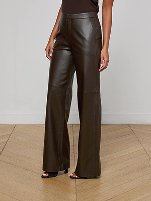 A person wears the L'AGENCE Livvy Leather Trouser—high-waisted, wide-leg chocolate pants—with a sleeveless black top, standing on a light wood herringbone floor. Their arms are relaxed by their sides, and their face is not visible.