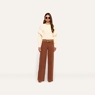 A person wears a cream cable-knit sweater with fringe detailing and high-rise cognac brown Scottie Corduroy Wide-Leg Pants with a belt.