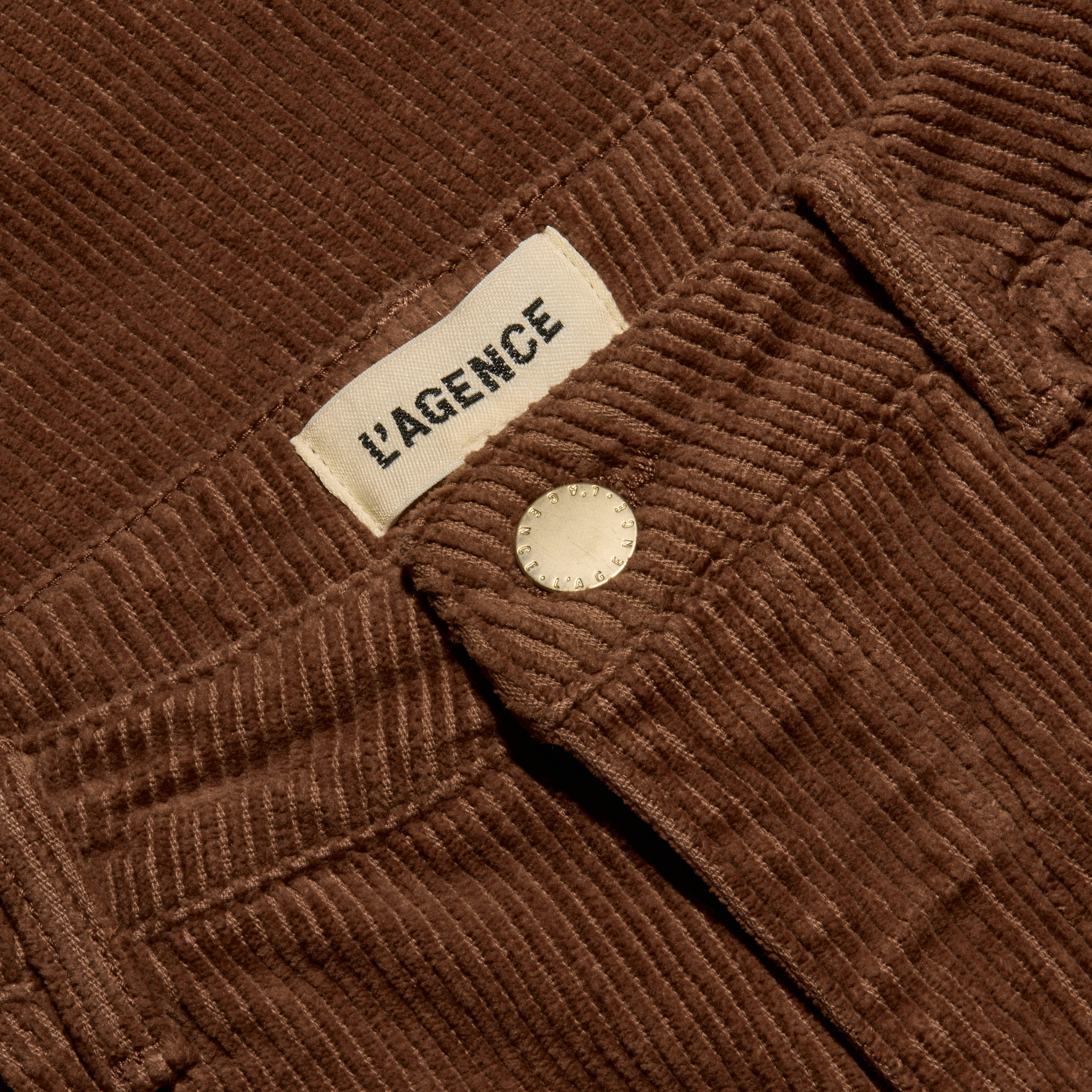 Close-up of cognac brown, high-rise Scottie Corduroy Wide-Leg Pant featuring a metal button and a label reading LAGENCE.
