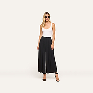 Woman wearing sunglasses, a white sleeveless top, Novalynn Cropped Pleated Pant in black, and black heeled sandals stands against a plain light background.