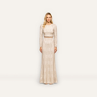 A woman stands against a plain white background, wearing the Zeta Sequin Maxi Skirt—a long, light-colored skirt adorned with subtle champagne-inspired sequin patterns. With her blonde hair and neutral expression, she presents an elegant look perfect for any special occasion.
