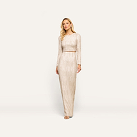 A woman models the Zeta Sequin Maxi Skirt, a floor-length design covered in shimmering champagne sequins, paired here with a coordinating long-sleeved top. She stands against a plain white background, gazing thoughtfully to the side. Perfect for special occasions, this skirt showcases elegant detailing inspired by the signature Zeta style.