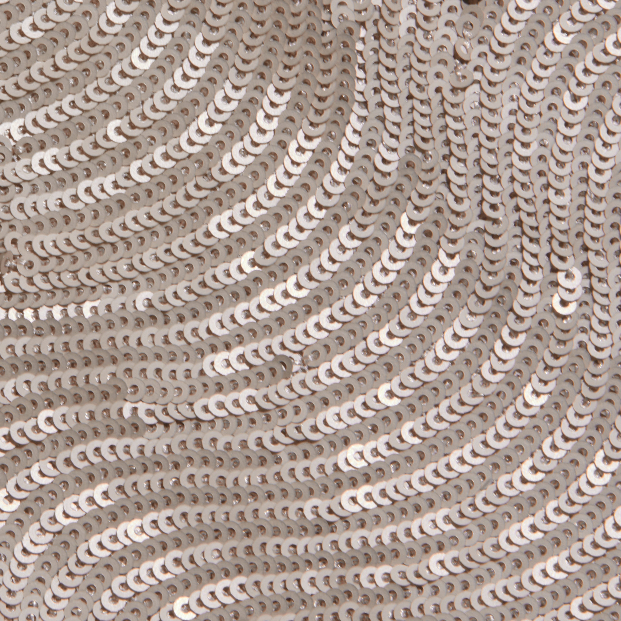 Close-up of shiny, champagne sequins sewn onto fabric in swirling, wave-like patterns creates a textured and reflective surface—perfect for special occasions or elevating your look with the elegant Zeta Sequin Maxi Skirt.