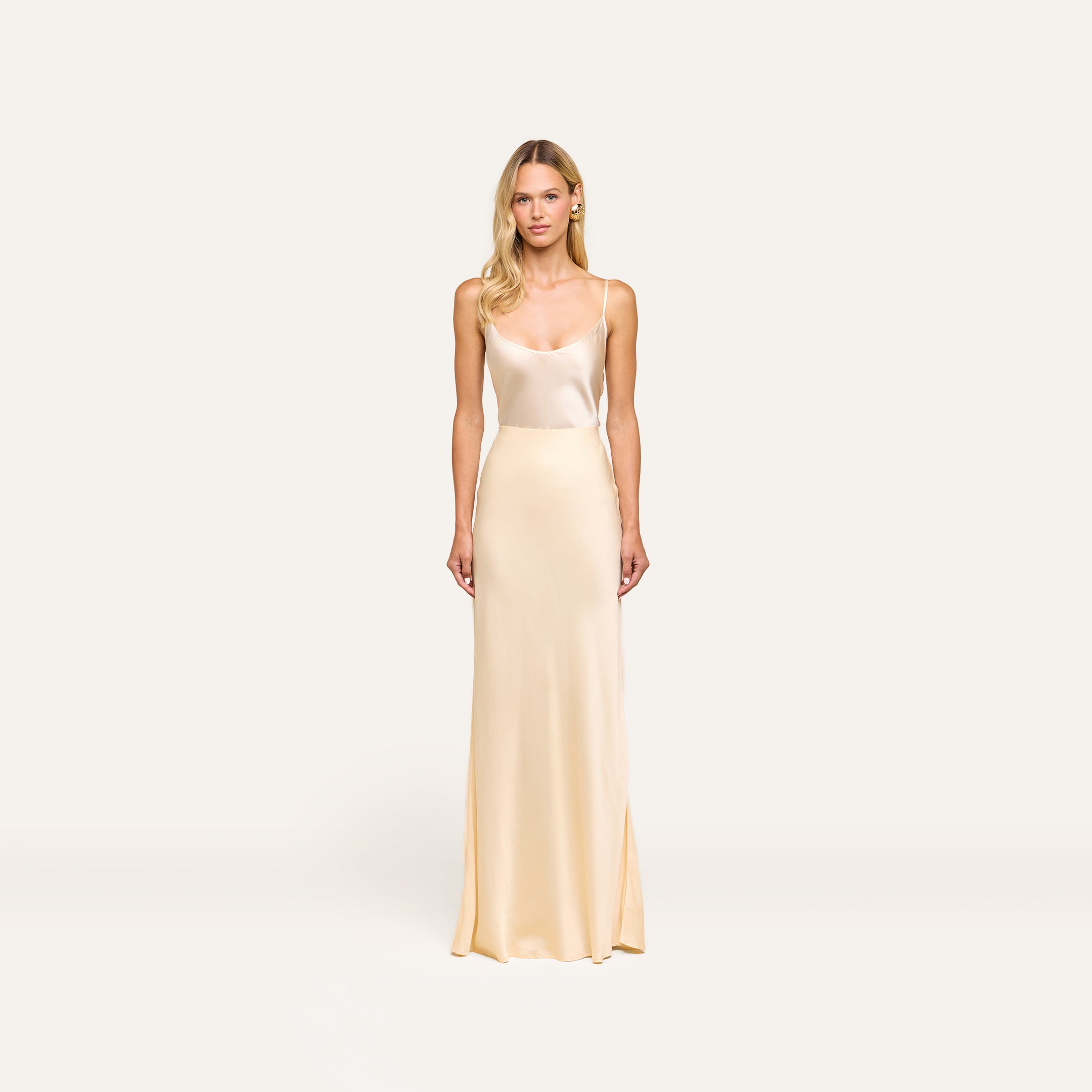 Woman wearing the Zeta Satin Maxi Skirt in cream, bias-cut with a satin finish, standing against a plain white background, facing forward with arms relaxed at her sides.