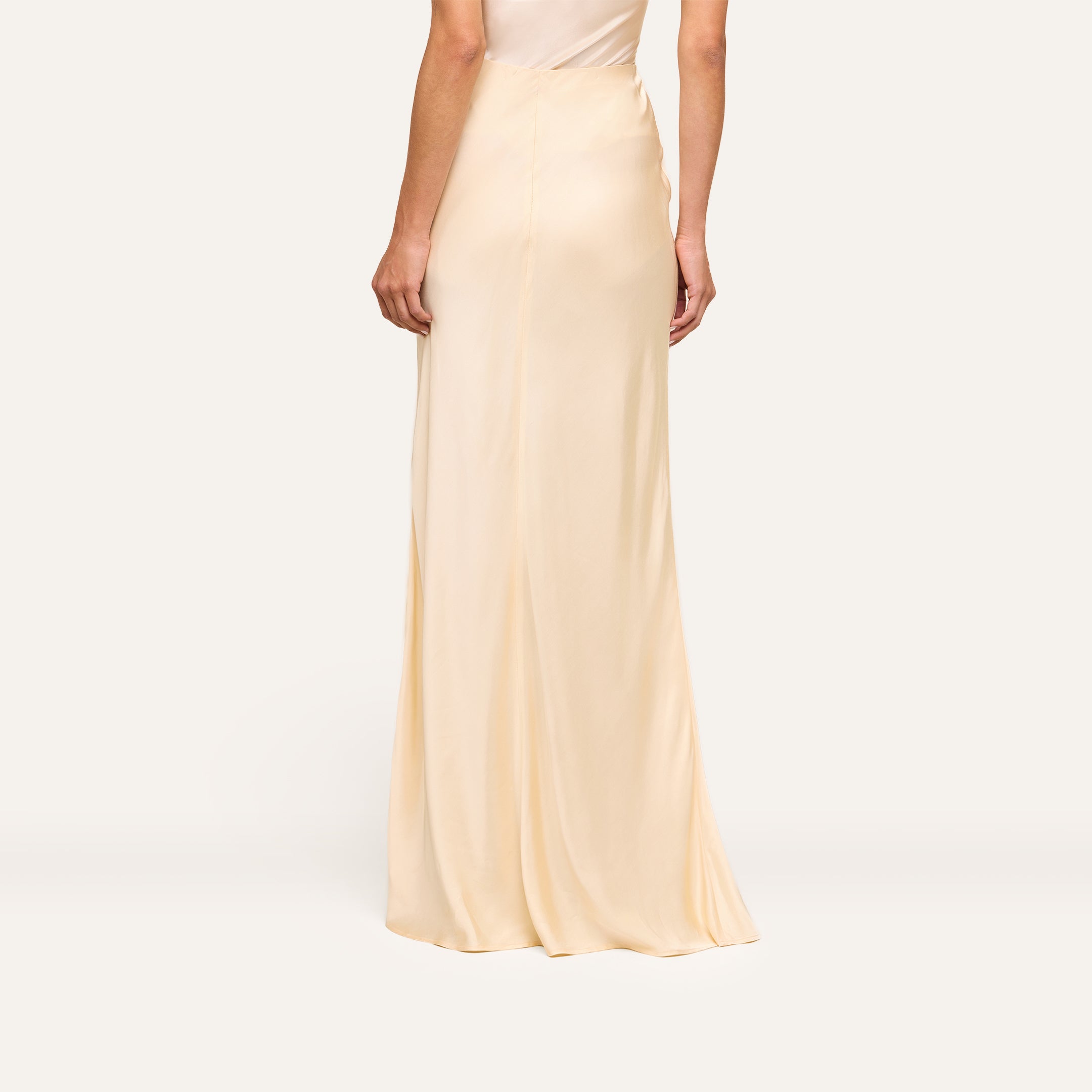 Wearing a long, light beige Zeta Satin Maxi Skirt, the person is shown from the back against a plain, light background.