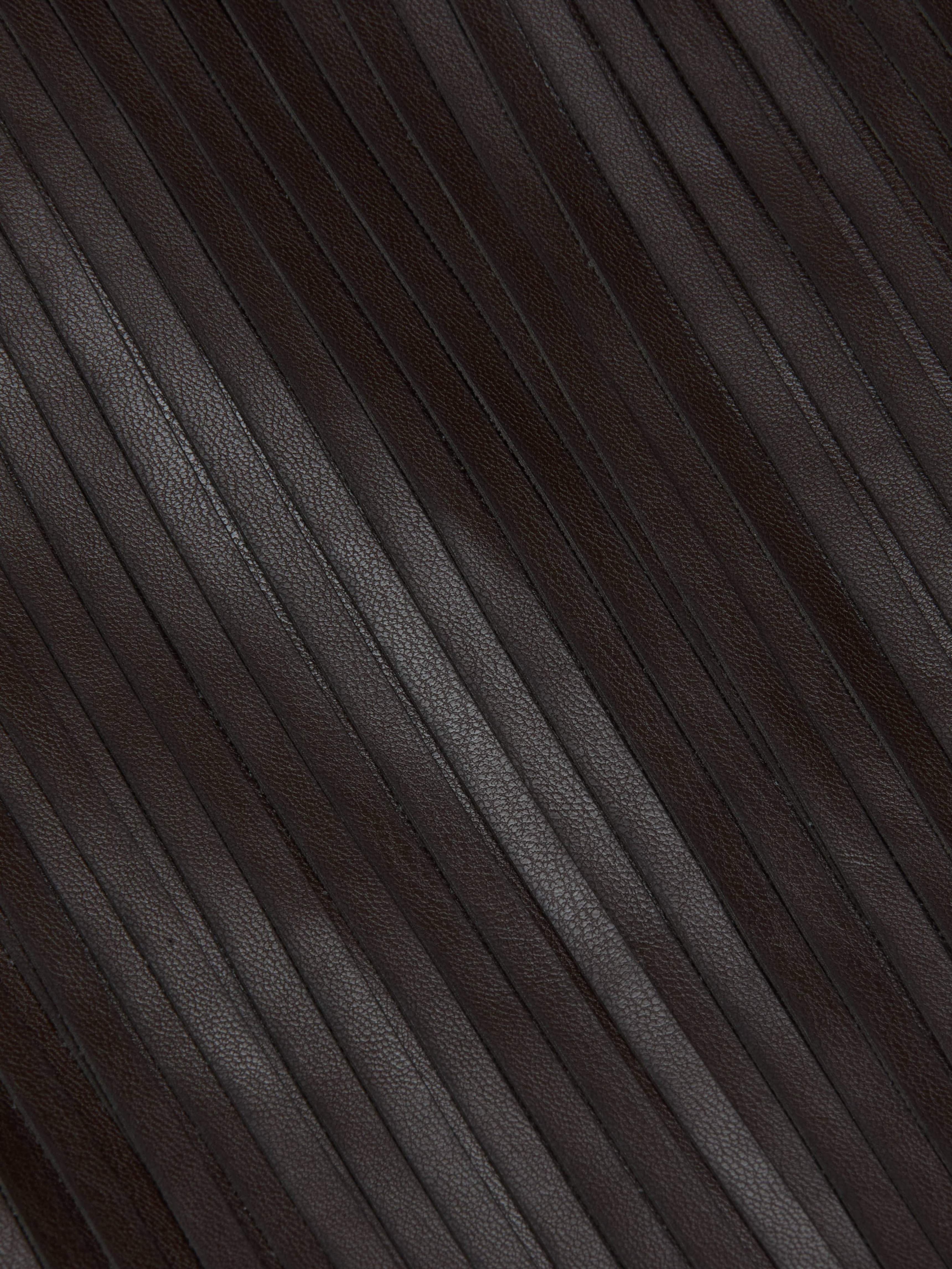 Close-up of the Karolina Fringe Skirt in dark brown vegan leather, featuring vertical pleated textured ridges and parallel seams. The surface is smooth with a slight gloss.