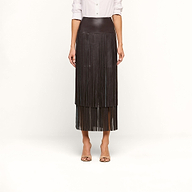 A person wearing a white shirt and the Karolina Fringe Skirt—a high-waisted, black vegan leather skirt with fringe—paired with open-toed heels, standing against a plain white background.