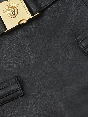 Close-up of the Yvette Vegan Leather Mini Skirt by L'AGENCE in black, showing a gold lion head clasp engraved with LA RENCE and two stitched leather details.
