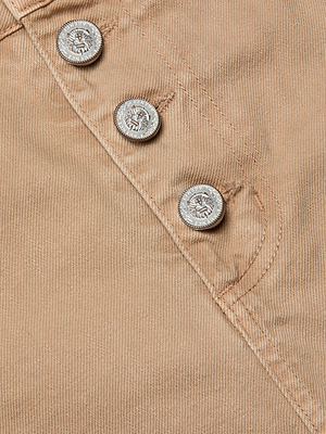 Close-up of all-cotton denim fabric with three silver VAGMINE-engraved logo buttons. Visible stitching outlines a pocket seam, highlighting the stylish Solene Jean Mini Skirt design.