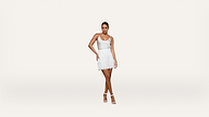 A woman stands against a plain white background, wearing a white sleeveless top, a white lace skirt, and white high-heeled sandals. She looks ahead with one leg crossed in front of the other.