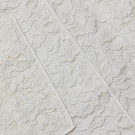 Close-up of the Riven Lace Mini Skirt’s semi-sheer lace fabric featuring a floral pattern and raised diagonal seams across its textured surface, perfect for an elegant look.