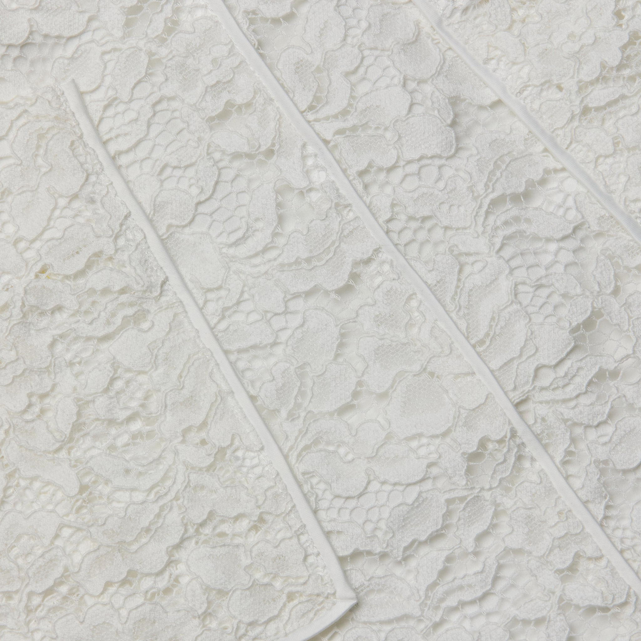 Close-up of the Riven Lace Mini Skirt’s semi-sheer lace fabric featuring a floral pattern and raised diagonal seams across its textured surface, perfect for an elegant look.