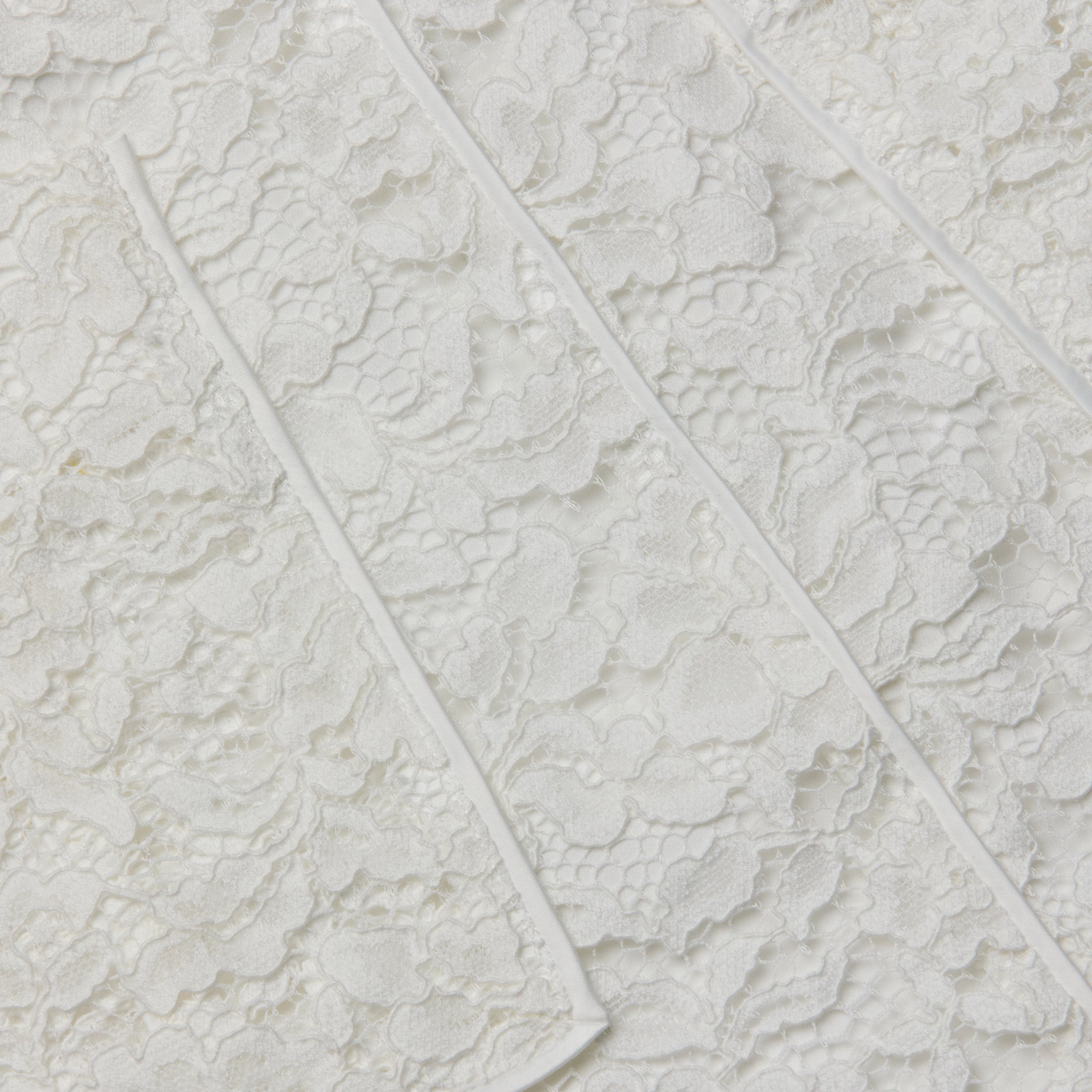 Close-up of the Riven Lace Mini Skirt’s semi-sheer lace fabric featuring a floral pattern and raised diagonal seams across its textured surface, perfect for an elegant look.