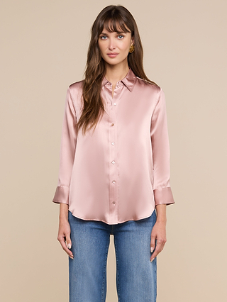 Une femme aux longs cheveux châtains porte un chemisier Dani Silk rose pâle, confectionné en charmeuse de soie à 100 , à manches trois-quarts, ainsi quun jean bleu ; elle se tient debout devant un fond beige uni.