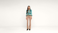 A woman stands facing forward against a plain white background, wearing a teal patterned blouse, beige pants, and black shoes.