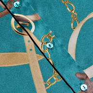 Close-up of the Dani Silk Blouse in teal, featuring shiny buttons and a printed pattern of gold chains and belts.