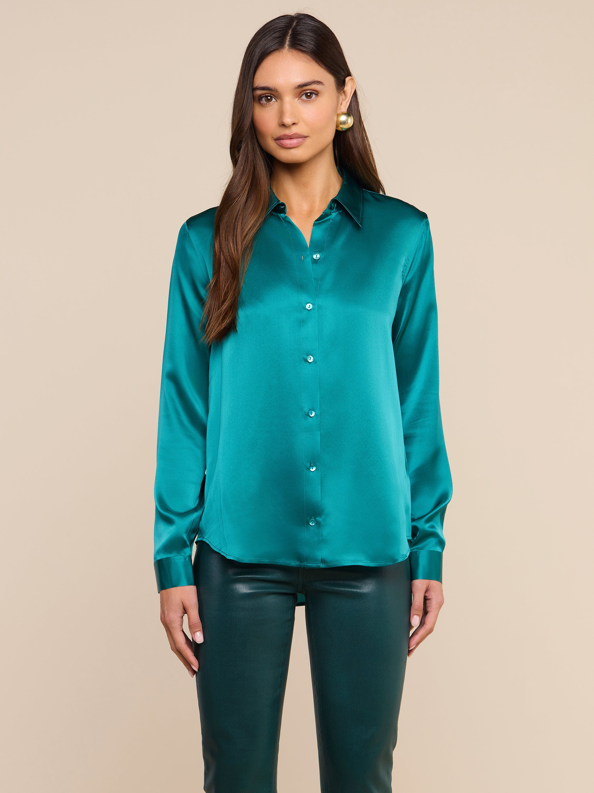 A woman with long brown hair wears the Tyler Silk Blouse in teal and matching teal pants, standing against a plain light background.