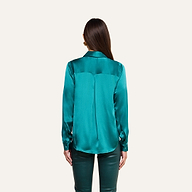 A woman faces away against a plain light background, wearing the Tyler Silk Blouse in teal with matching teal pants. Her straight brown hair is loose, and her arms rest by her sides.