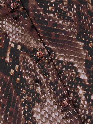 Close-up of the Tyler Silk Blouse by L'AGENCE, featuring brown and black snake print fabric with shiny brown buttons sewn diagonally across the material.