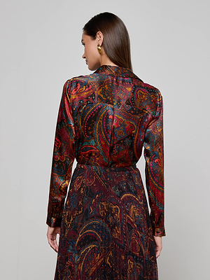 A woman with long brown hair, wearing gold earrings and the L'AGENCE Tyler Silk Blouse, stands with her back to the camera against a plain light gray background.