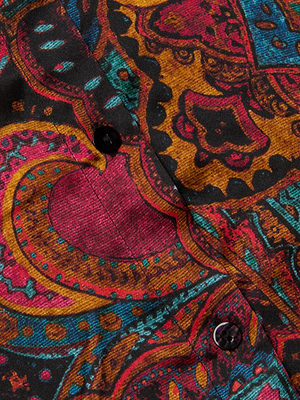 Close-up of the Tyler Silk Blouse by L’AGENCE, a button-down long-sleeve shirt with a vibrant paisley print in red, orange, teal, and black. Features two black buttons and showcases intricate swirling shapes in bold colors.