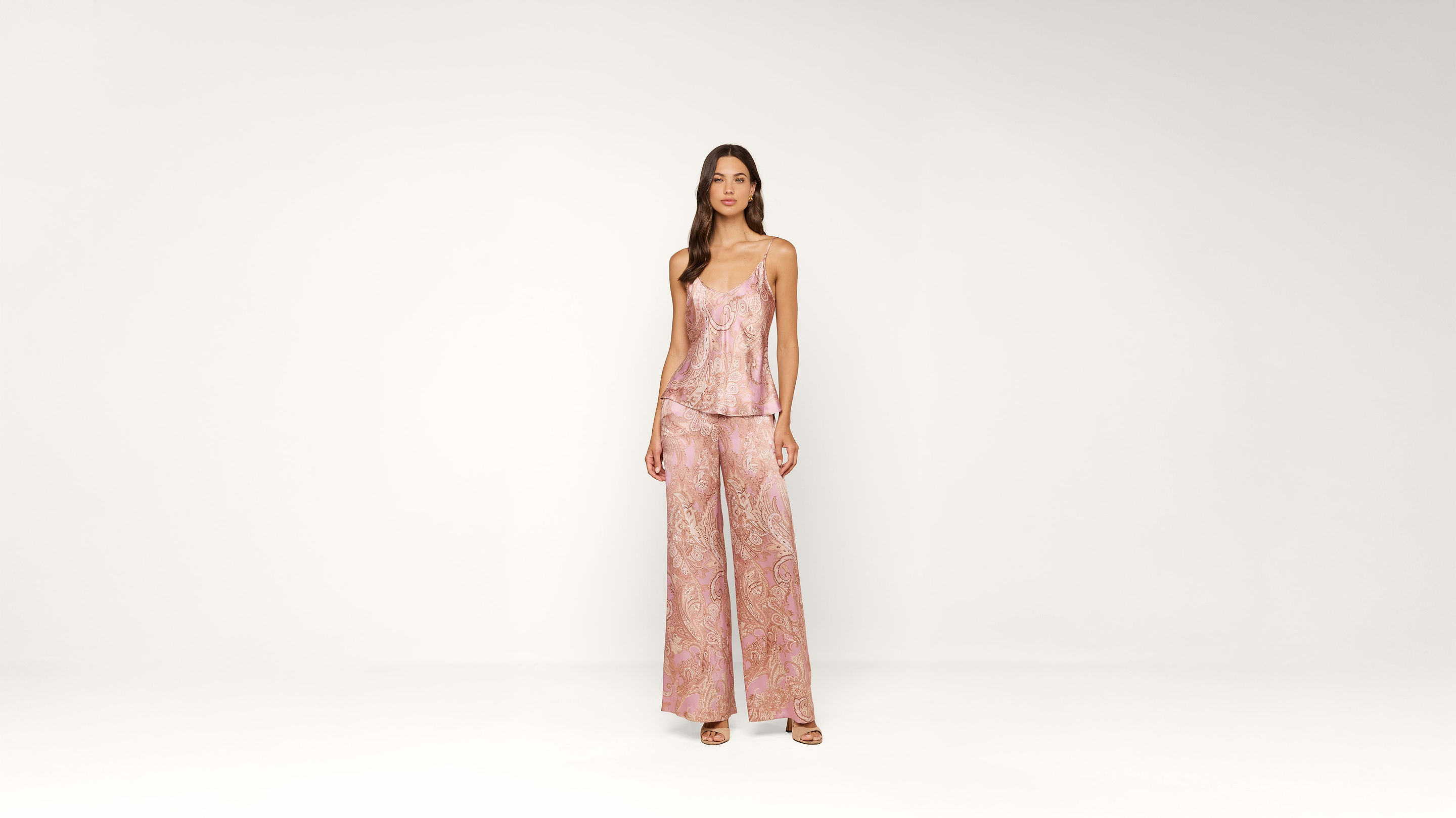 Woman standing against a plain white background, wearing a pink paisley-patterned sleeveless top and matching wide-leg pants, with open-toe heels.