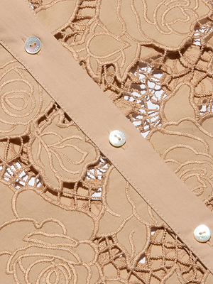 Close-up of beige lace with rose patterns and openwork, plus a solid beige strip with shiny white buttons. This detailed fabric pairs perfectly with the Seychelle Cropped Eyelet Blouse for a stylish look.