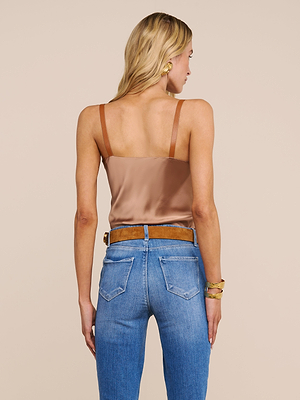 Une femme aux longs cheveux blonds est représentée de dos, portant la camisole Lux Silk Buckle-Strap Camisole en marron, un jean taille haute bleu, une ceinture marron, des boucles doreilles en or et un bracelet en or sur un fond beige.