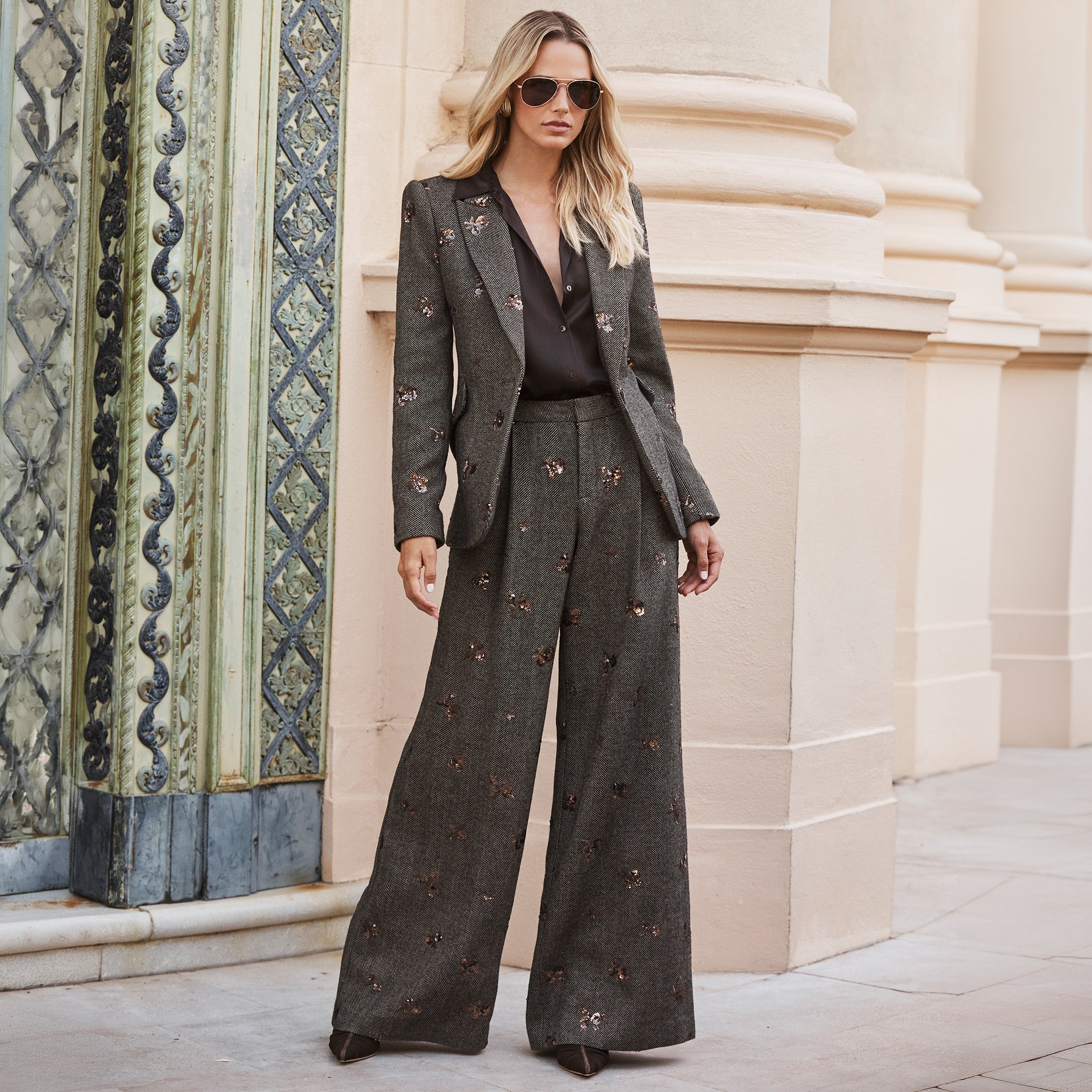 A woman wears a dark blazer and Allanah Sequined Trousers featuring a straight-cut herringbone pattern with floral motifs over a black collared shirt.