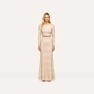 A woman wearing the Rogan Sequin Top, a light beige long-sleeve blouse embellished with champagne sequins, stands facing forward against a plain, light background for a party-ready look.