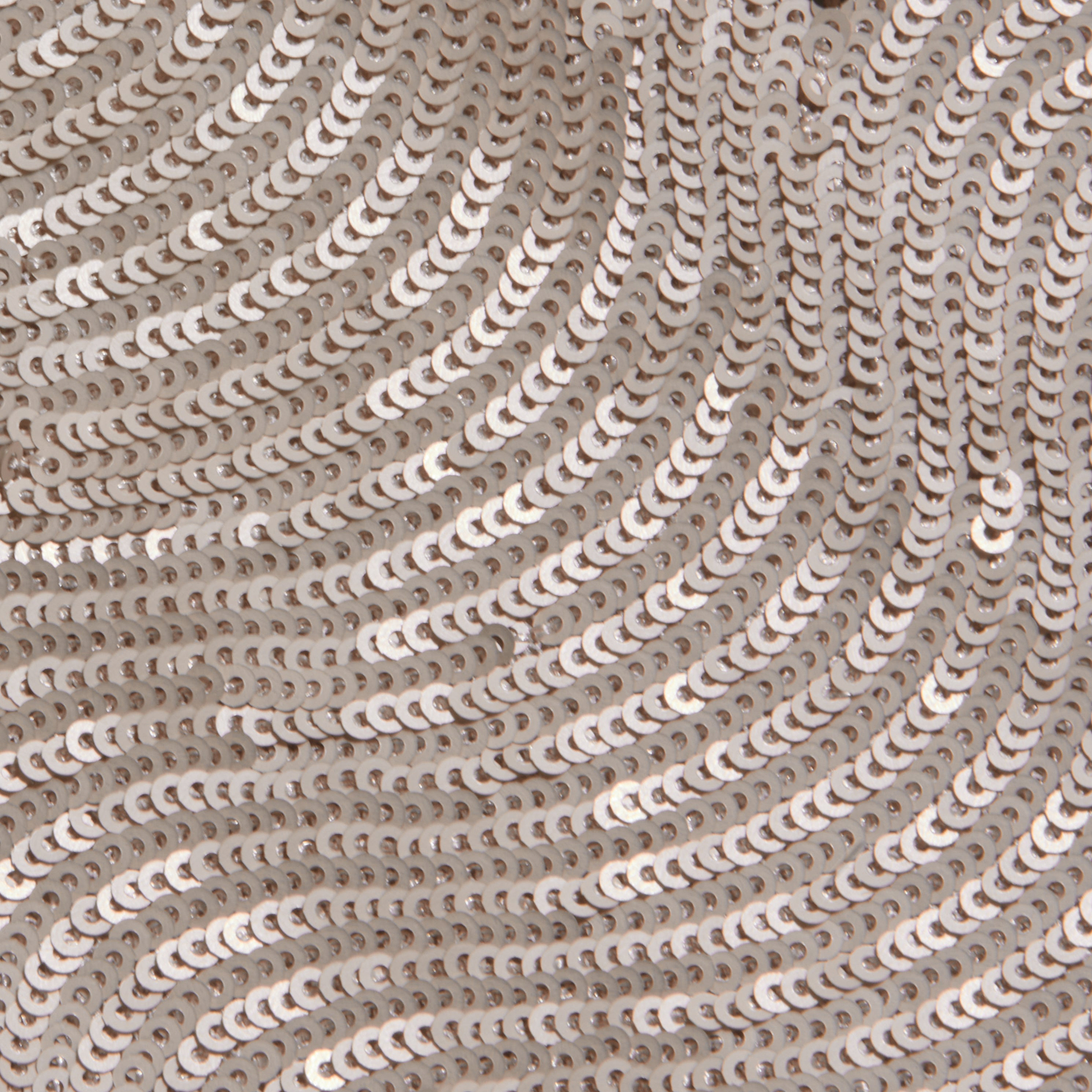 Close-up of the Rogan Sequin Top, featuring party-ready, shiny silver sequins sewn in swirling wave-like patterns on a light fabric background.