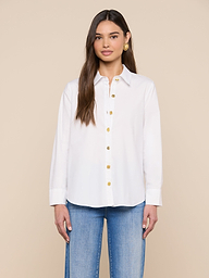 Une femme aux longs cheveux bruns porte la chemise à boutons Ellery dans une coupe décontractée, associée à un jean bleu clair. Elle se tient debout sur un fond beige uni, de face, avec une expression neutre et les bras détendus le long du corps.