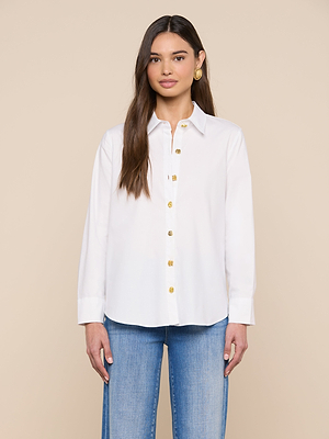 A woman with long brown hair wears the Ellery Button-Down Shirt in a relaxed fit, paired with light blue jeans. She stands against a plain beige background, facing forward with a neutral expression and relaxed arms at her sides.