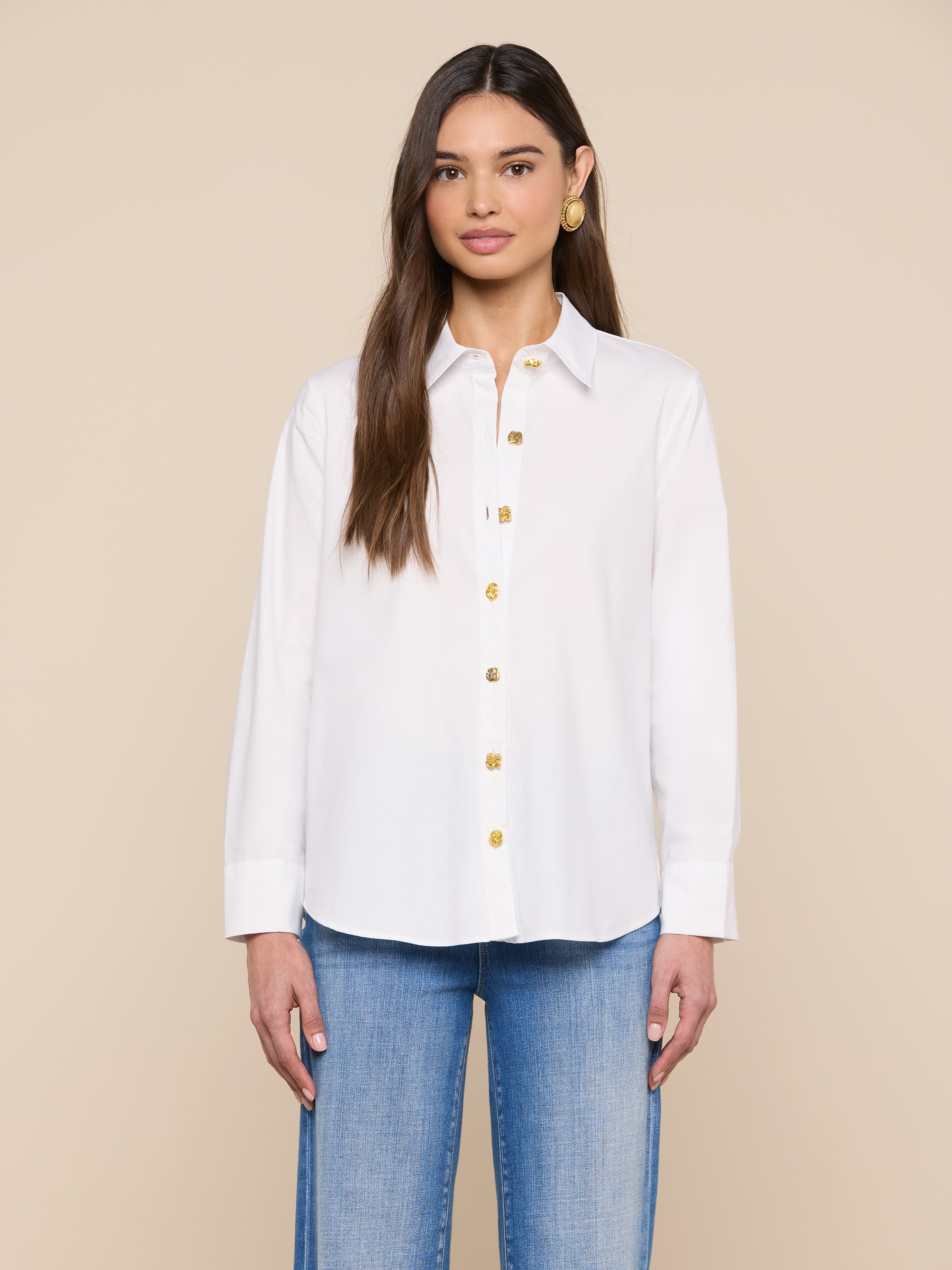 Une femme aux longs cheveux bruns porte la chemise à boutons Ellery dans une coupe décontractée, associée à un jean bleu clair. Elle se tient debout sur un fond beige uni, de face, avec une expression neutre et les bras détendus le long du corps.
