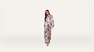 Woman wearing a pink floral off-shoulder jumpsuit and heels stands against a plain white background, facing forward with a relaxed expression and long hair down.
