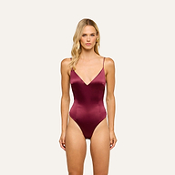 A woman wearing the Dara Stretch-Satin Bodysuit in deep burgundy, featuring adjustable straps, stands against a plain, light background, facing forward.