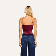 A woman with long blonde hair is facing away, wearing the Dara Stretch-Satin Bodysuit in burgundy, which features adjustable straps, paired with high-waisted dark blue jeans. The background is plain and light-colored.