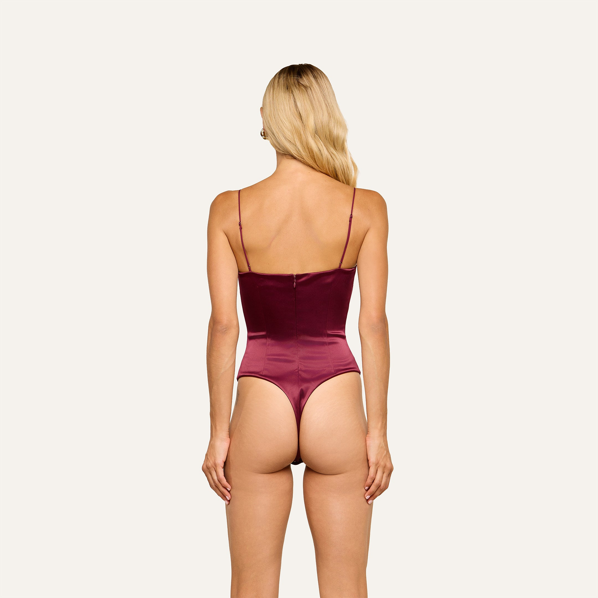A woman with long blonde hair is shown from the back, wearing the Dara Stretch-Satin Bodysuit in burgundy with adjustable straps against a plain light background.