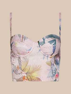 The Sonya Bustier is a cropped top with thin straps, made from lightweight twill and decorated with pastel palm leaf and tropical flower prints on a light pink background.
