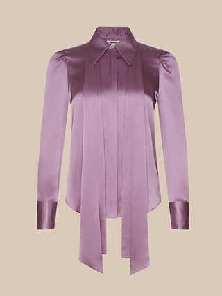 The Honey Silk Blouse is a long-sleeve, shiny mauve silk charmeuse top featuring a pointed collar, button-down front, and two wide neckties that drape down. This tie-neck blouse has slight puff shoulders and fitted cuffs, displayed against a light beige background.