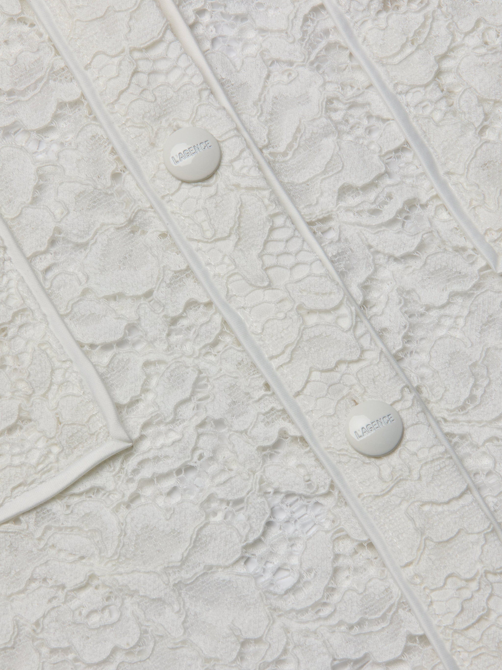 Close-up of the Roelle Lace Blouse in white, showcasing its intricate floral lace patterns, two white buttons engraved with “LARENTE,” and delicate piping details. The romantic texture and fine design elements of this blouse are clearly visible.