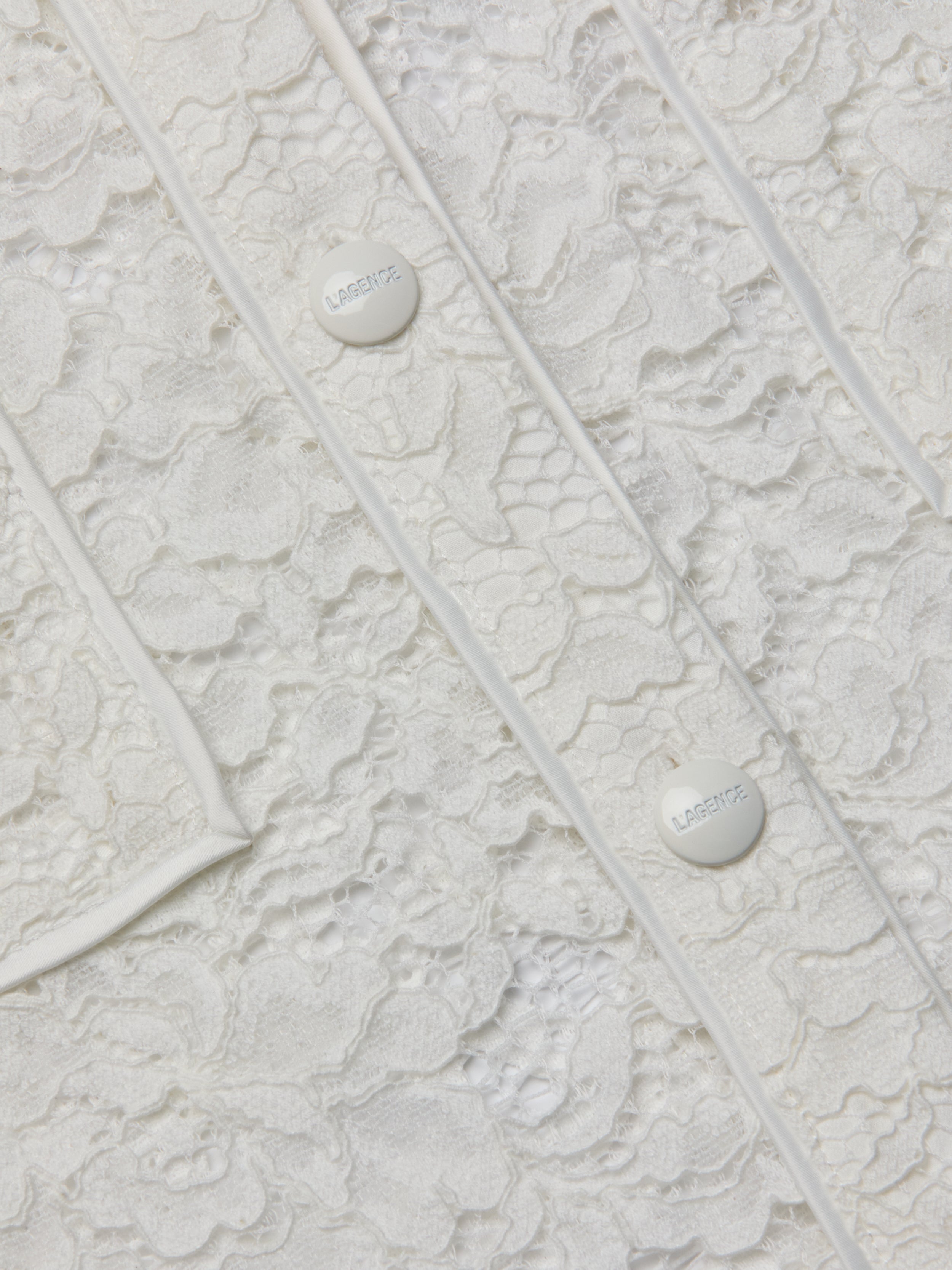 Close-up of the Roelle Lace Blouse in white, showcasing its intricate floral lace patterns, two white buttons engraved with “LARENTE,” and delicate piping details. The romantic texture and fine design elements of this blouse are clearly visible.