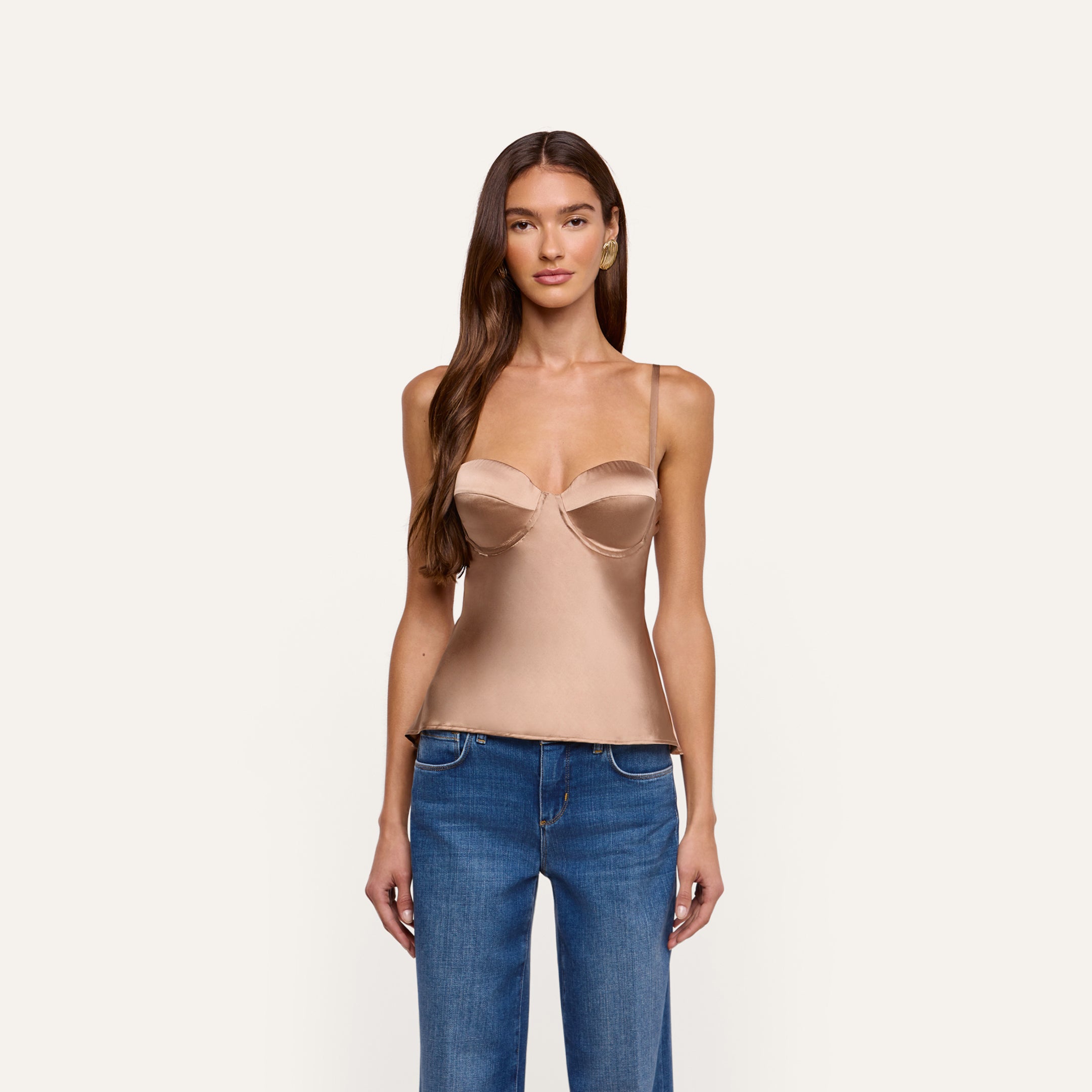 A person wearing an Orlina Silk Camisole, a beige, silk charmeuse corset-style top with thin straps, paired with blue jeans.