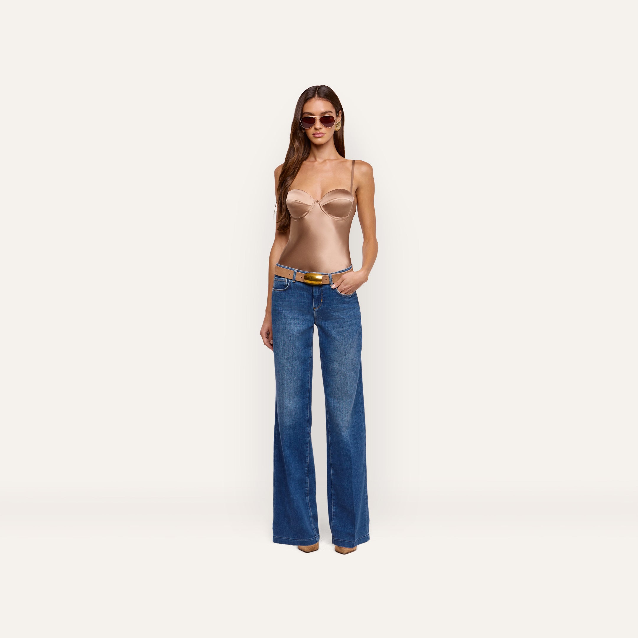 A woman wearing an Orlina Silk Camisole with underwire cups, wide-leg blue jeans, a tan belt with a gold buckle, and sunglasses.