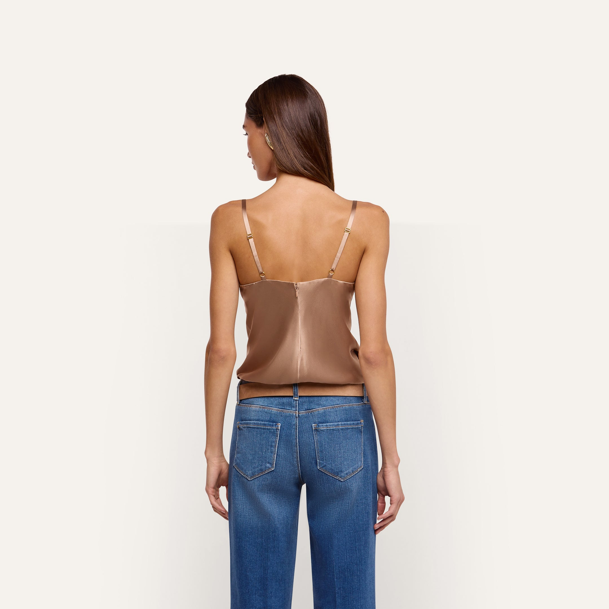 Back view of a person wearing a beige silk charmeuse Orlina Silk Camisole with thin straps and underwire cups, paired with blue jeans.
