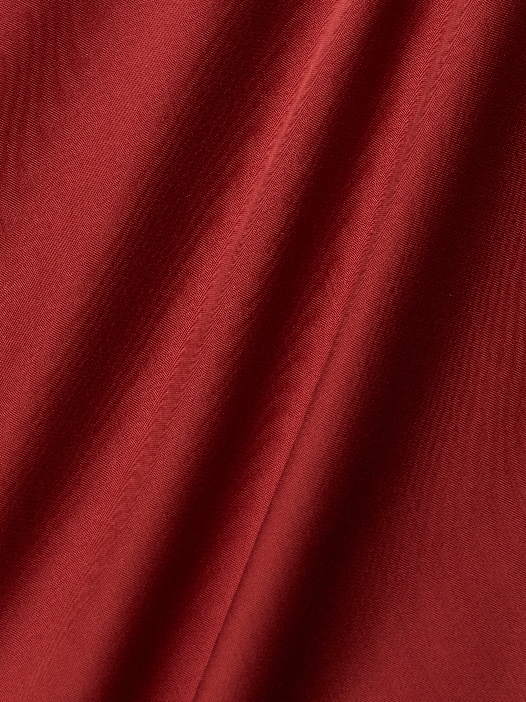 Close-up of the Eddie Tank in poppy red, showcasing its smooth, bias-cut satin fabric with soft folds and diagonal lines created by gentle draping. The texture appears soft and slightly shiny, highlighting the richness of the color.